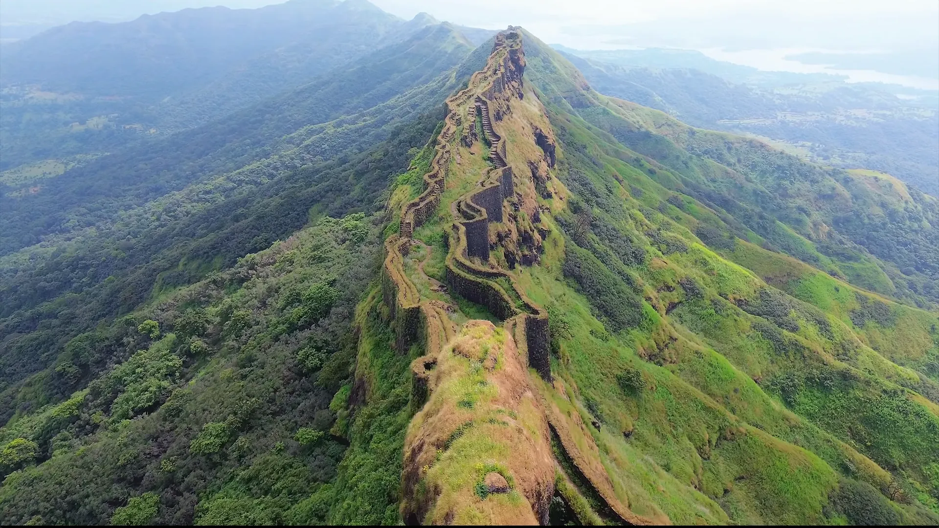 The stone walls of Rajgad Fort running along a green Sahyadri ridge, near the farmstay.