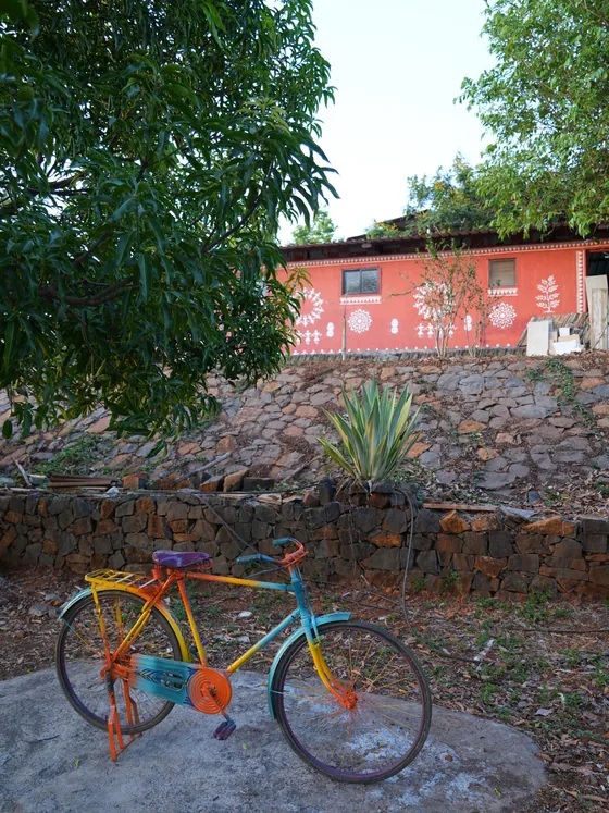 A rainbow-painted bicycle below a stone wall and a mural-covered building.