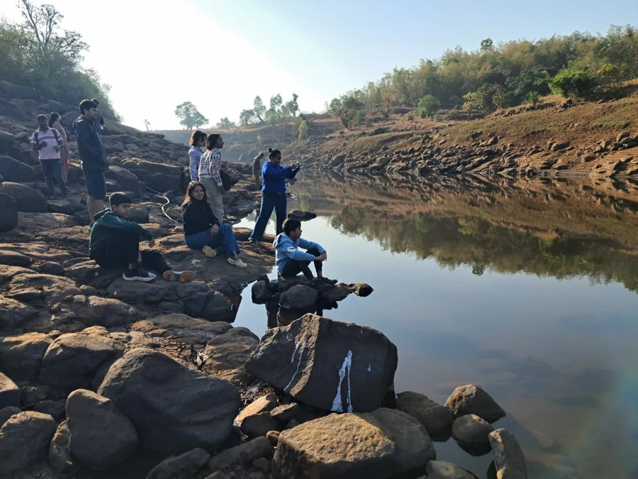 A group sitting out on the rocks by the river below the farmstay, early in the morning, with the water flat and still.