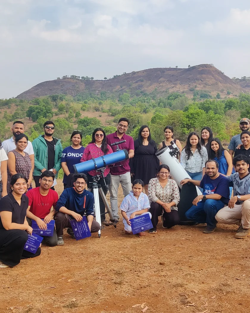 A group of past guests with two telescopes on the farm, some holding their certificates, the hills behind.