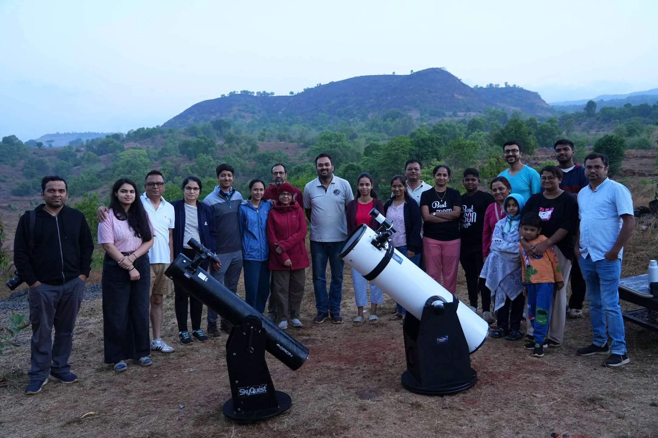 A past stargazing group gathered on the farm by daylight with two telescopes, the hills behind them.