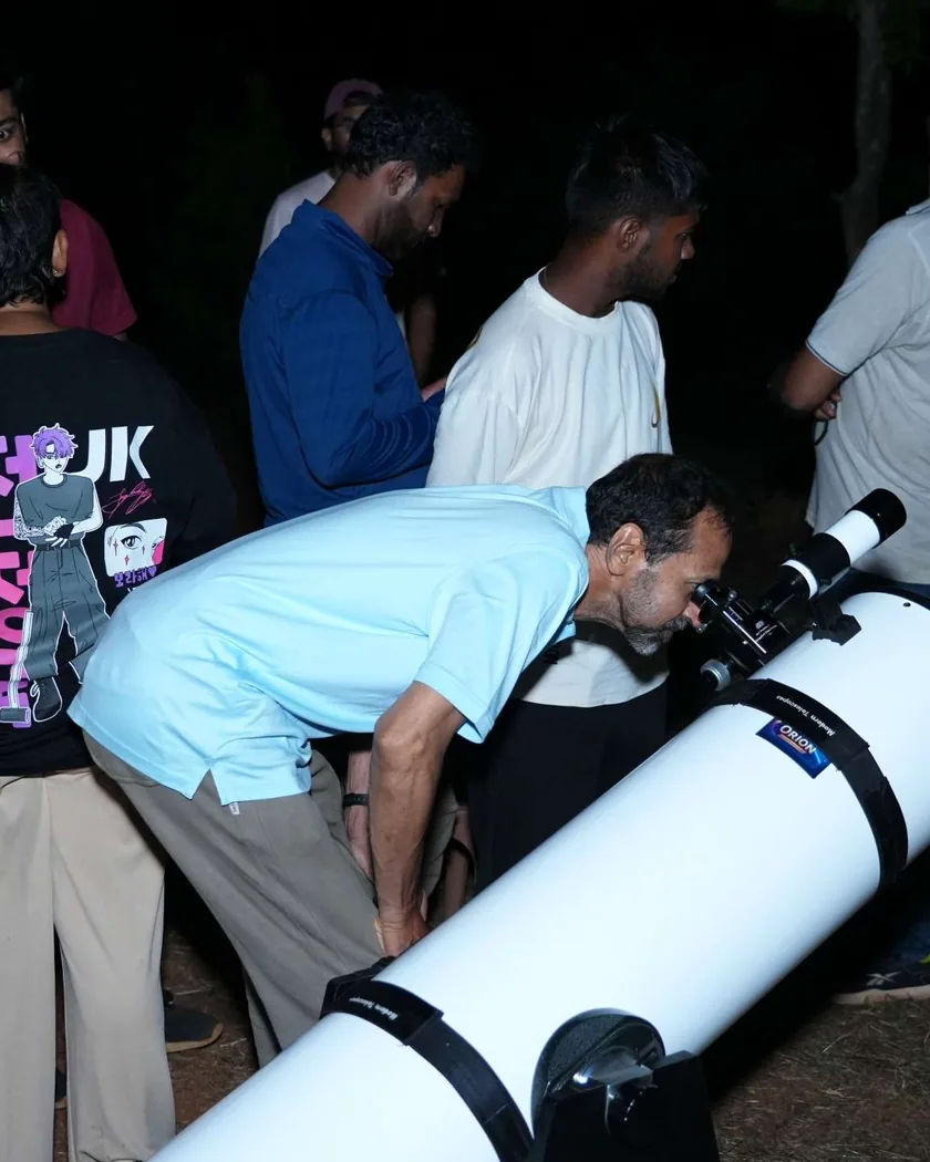 A guest bending to the eyepiece of a large white telescope at night, others waiting their turn.