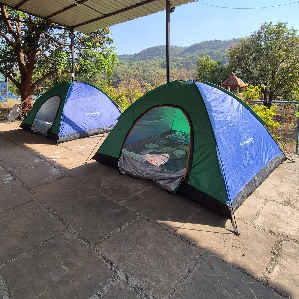 Two dome tents pitched on stone under an open shelter, trees and hills beyond.