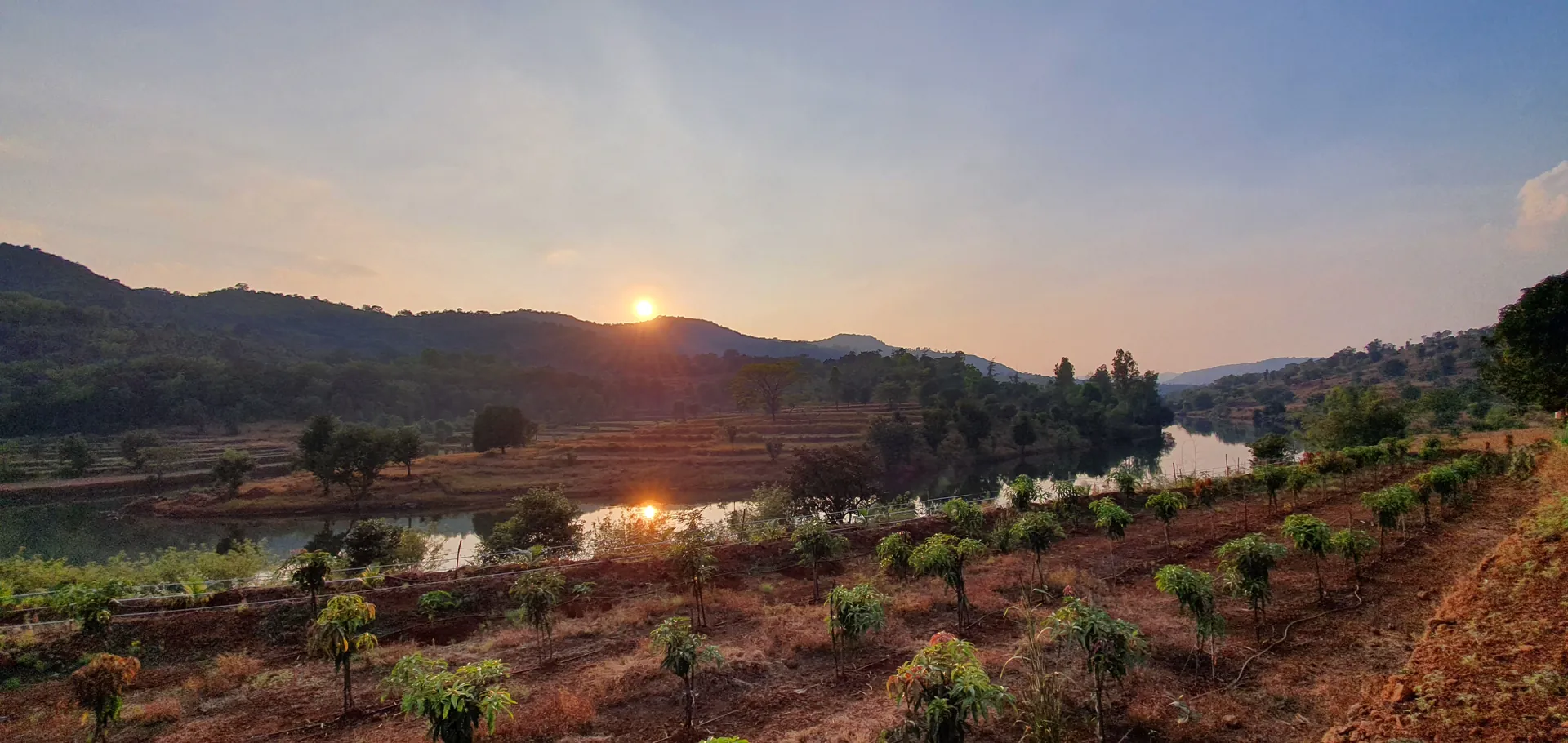 The sun going down over the hills, reflected in the river below the farm.