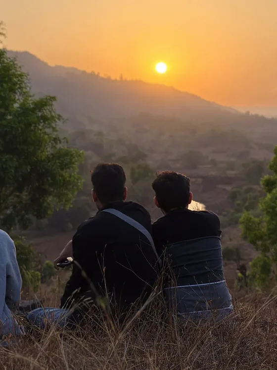Three people sitting on the hillside, watching the sun go down over the hills.
